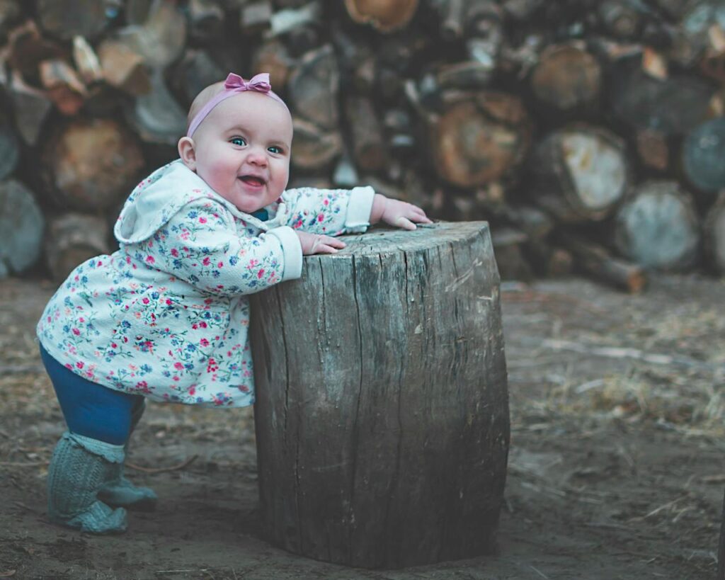 um bebê em pé escorado em um tronco de arvore